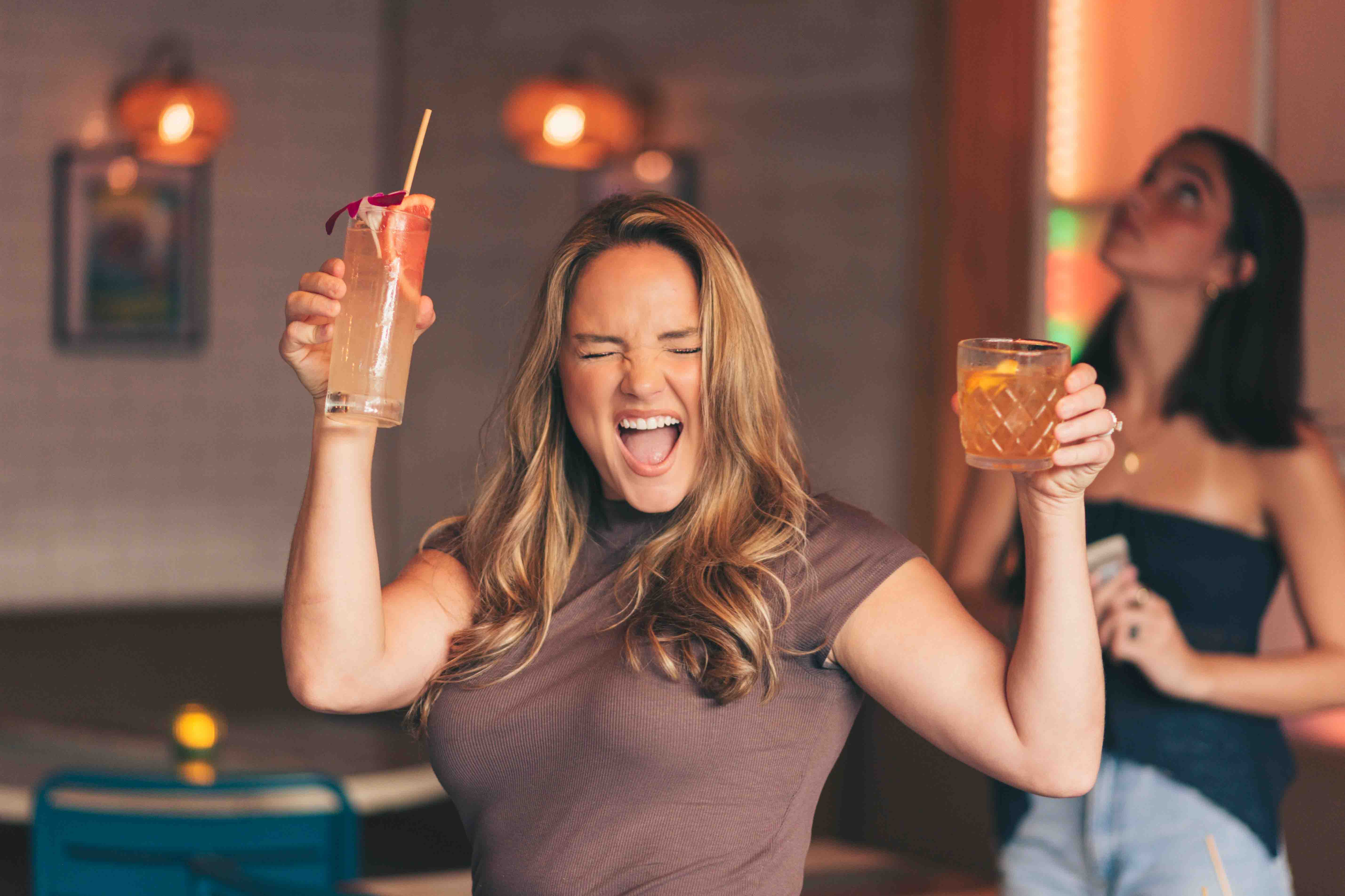 A guest celebrating with two cocktails raised at Zunzibar